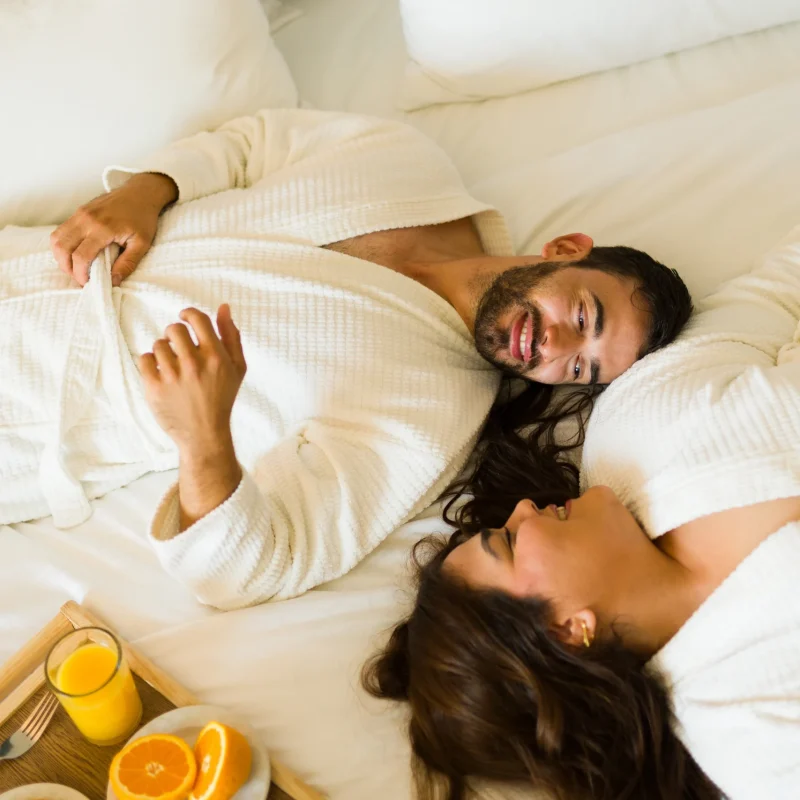 smiling girlfriend hugging boyfriend in bathrobe with glass of juice